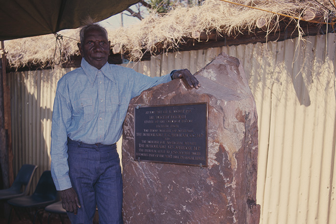 Aboriginal man standing next a plaque set into a large piece of rock