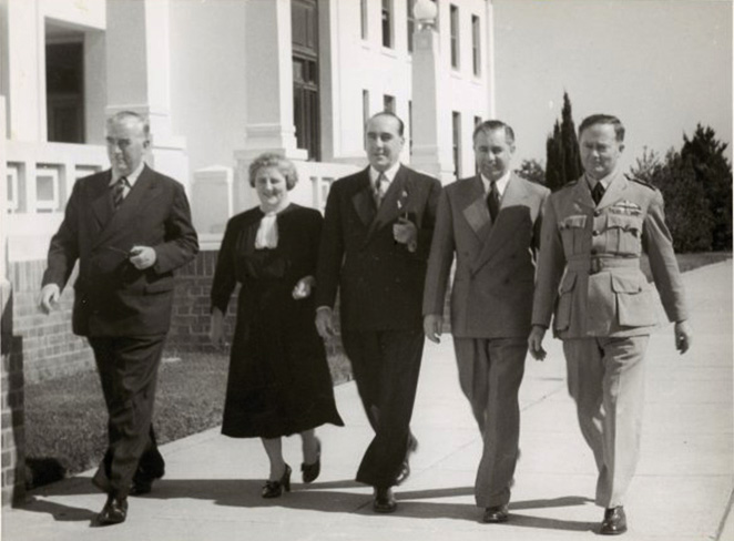 Four men and a woman walking abreast along the front of Old Parliament House.