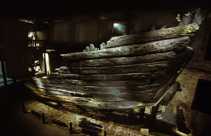 The prow or stern of a timber vessel illuminated in a two-storey exhibition hall