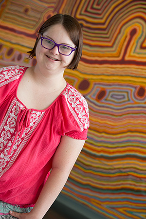 A girl standing in front of an Aboriginal artwork.