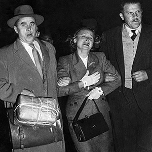 Photo taken at night showing distressed woman flanked by two men in suits holding her arms