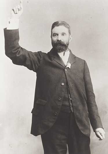 studio photo of man with dark beard posing as though he is addressing a crowd