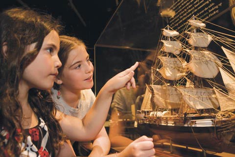 Two girls look at a model of a sailing ship.