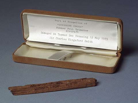 Wooden fragment with 'Southern Cross 12.5.35' printed on one side. The fragment is stored in a Parker Pen box covered in yellow fabric, with a typed note attached to the inside lid.