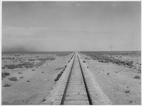 Black and white photograph of a straight section of railway line, surrounded by desert.