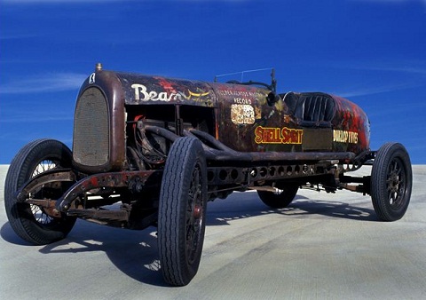 A four-wheeled open seater car with a long engine cowling, boat tail and low glass windscreen. 'Bean' has been painted in white on the top right of the bonnet cover. The words 'Shell Spirit' and 'Dunlop Tyres' are visible on the right side of the car's body.