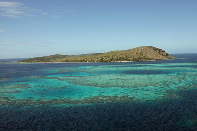 Aerial photo of a small island with reef in foreground.