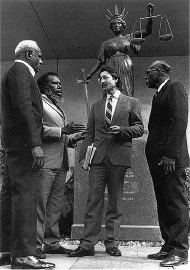 Four people standing in front of a statue of Lady Justice.