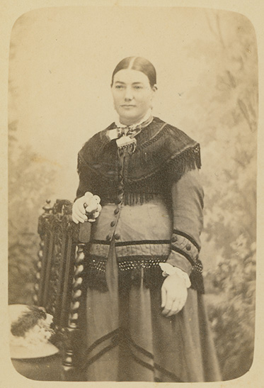 A young pregnant woman posing with hand resting on back of a chair.