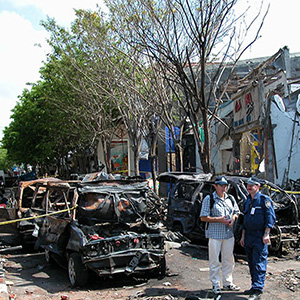 two AFP officers confer in the street. Behind them are the burnt-out remains of vehicles and a wrecked building