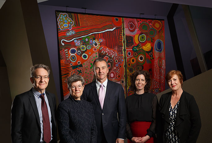 Group portrait of men and women standing in front of a painting