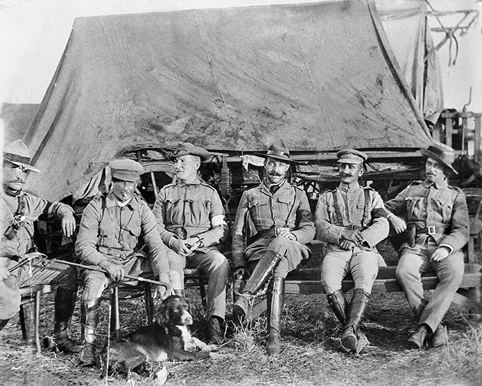 six men in uniform sitting down in front of tent