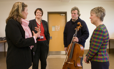 A man holding a cello stands talking to three women.