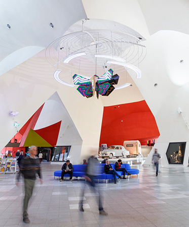 Image showing the interior of a building with people moving through the space and a colourful moth sculpture hanging from the ceiling.