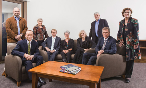 A colour photograph of the Museum's Council comprising five men and four women. Five are seated behind a coffee table, four are standing behind those seated.