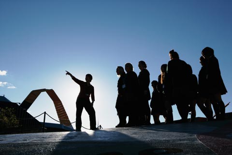 A group of visitor services hosts silhouetted in the Garden of Australian Dreams. One host stands slightly apart from the others, pointing out a feature of the space.