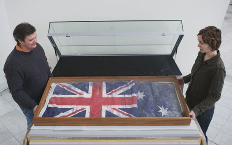 Patrick Baum and Antonia Ross prepare to move an Australian flag into a display case in the Museum's Hall