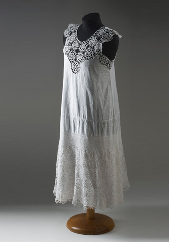 A white, cotton, sleeveless nightdress. The yoke of the nightdress is made from medallion crochet featuring a flower motif. The body of the nightdress is decorated with drawn thread work and the hem features a scalloped edge. A panel of crochet has been placed around the lower part of the nightdress.