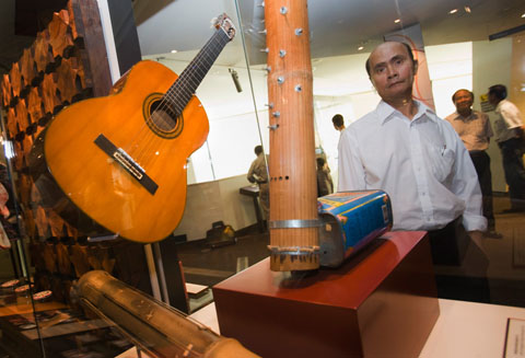 A man looks through a display case which contains a guitar and a bamboo musical instrument.