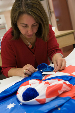 Conservator Carmela Mollica removes the adhesive residue from the double-sided tape used to adhere the jockey silks to a backing board before placing them into a frame.