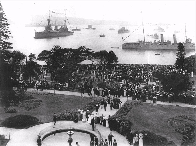 Two of that fleet unit’s warships and several smaller ones in background, with hundreds of people looking on from a park, possibly the Botanic Gardens.