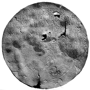 A battered disc, much worn and with holes in it. Words are visible, neatly inscribed in capitals in the top two thirds of the plate.