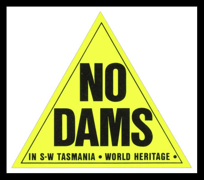 Yellow triangle on black background. Within the triangle are the words NO DAMS in capital letters. Beneath these are the words ‘IN S W TASMANIA. WORLD HERITAGE.