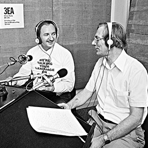 two men sitting in a radio studio in front of microphones. They are smiling and clearly in conversation. The present is wearing a top saying ‘We’re talking your language on 3EA’