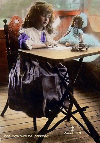 A postcard featuring a coloured photograph of a girl seated at a table with a doll on the table, and a message on the back. The text on the front reads '200. WRITING TO MOTHER'.