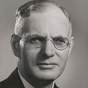 studio black and white photo of Curtin. He is wearing a dark suit and glasses