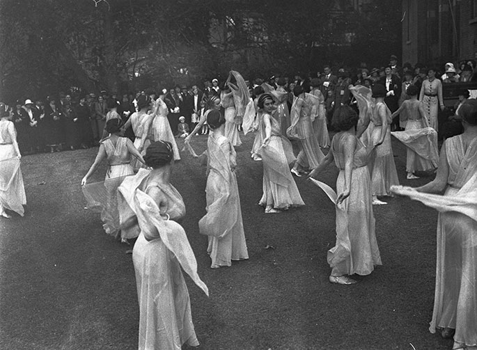 Photo taken from the rear of the stage with audience in the background. The 20 or so dancers are all wearing flowing white dresses