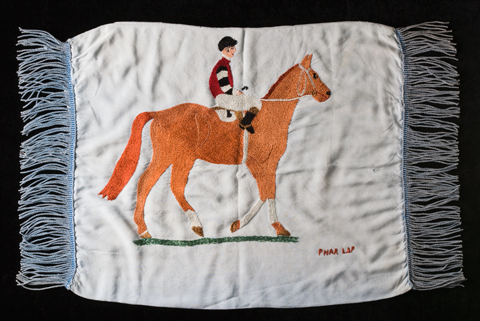 A cushion cover with an embroidered image of a horse and rider at the centre. 'Phar Lap' is stitched in red in the bottom right.