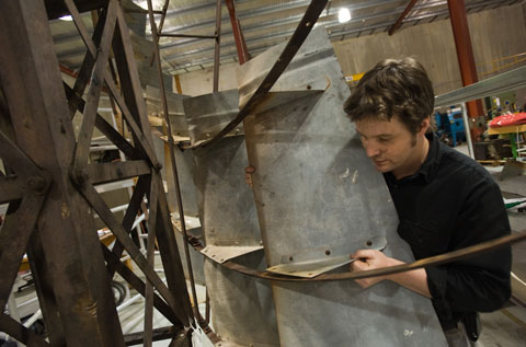 A man peers around a piece of galvanised steel, moving it into position on a large metal frame.