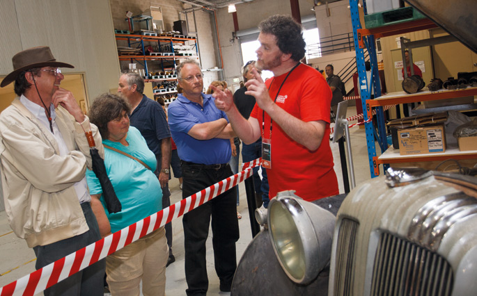 A photograph of three people looking on while a person standing behind the striped tape gives a talk.