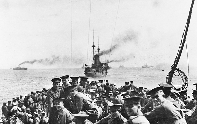 Grainy black and white photo taken on board a boat full of Australian soldiers, with ships in background