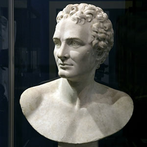 White bust of Cook against a blue background. Cook is shirtless and hatless with curled hair, in the manner of an ancient Greek hero