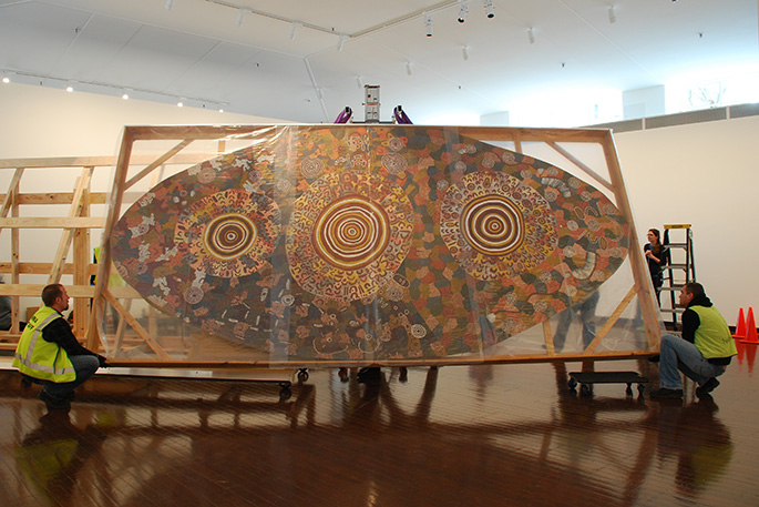 Two men holding a wooden frame containing an artwork.