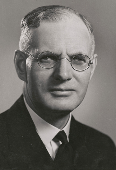 studio black and white photo of Curtin. He is wearing a dark suit and glasses