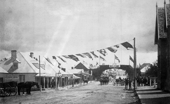 main street of small town with a horse and cart in foreground and a handful of people in the background. Bunting is suspended from poles
