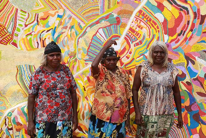 Three women standing in front of a painting.