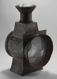 Black-coloured lamp with light metallic casing and circular glass panel at the front.