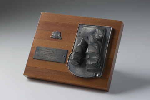 A small metal relief replica of the Sydney Opera House, plaque and the Australian coat of arms, on a polished timber base