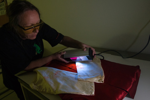 Conservator Deb Spoehr uses ultraviolet light to investigate staining on racing silks worn by the jockeys of Gaulus and the Grafter in 1897 and 1898 Melbourne Cup races.