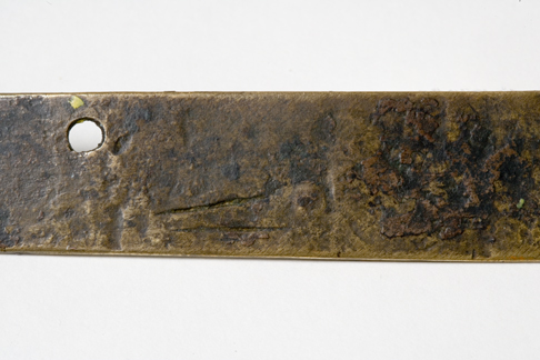 Close up image of a section of the back of the Leichhardt nameplate detailing the two score marks at the bottom close to the centre and the fastening hole at the top in the centre.