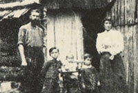 Black and white photograph showing a settler family outside a slab hut.