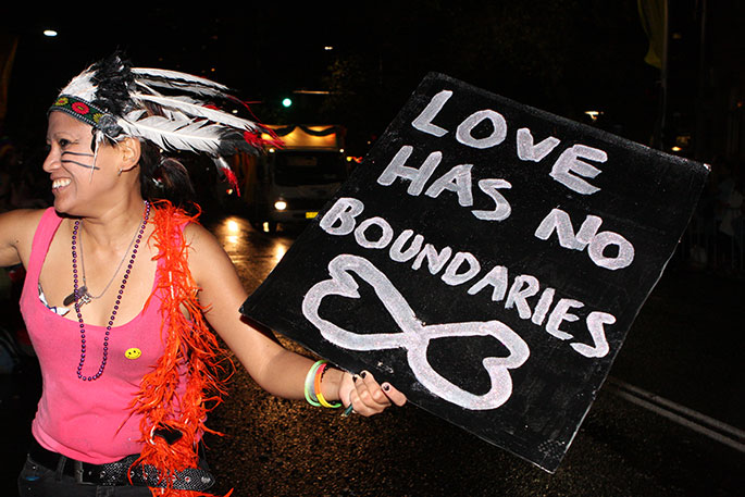 Woman in feathered headdress holding placard saying 'Love has no boundaries'