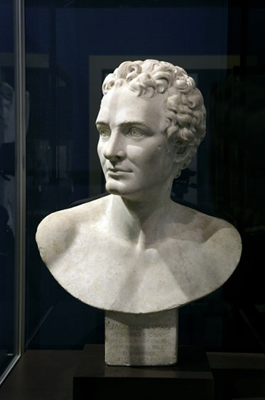 White bust of Cook against a blue background. Cook is shirtless and hatless with curled hair, in the manner of an ancient Greek hero