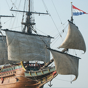 Timber sailing vessel at sea with lower sails catching the wind. The Dutch flag sails from the bowsprit.