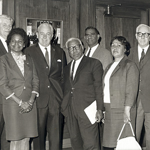 The seven people named stand in front of a wood-panelled wall in what looks like Old Parliament House.
