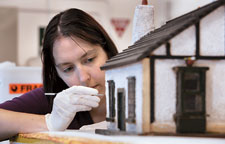 Conservator Cathy Collins preparing a 1930s doll's house for the Captivating and Curious exhibition.